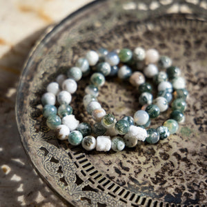Stack of moss agate crystal bracelets on a metal tray