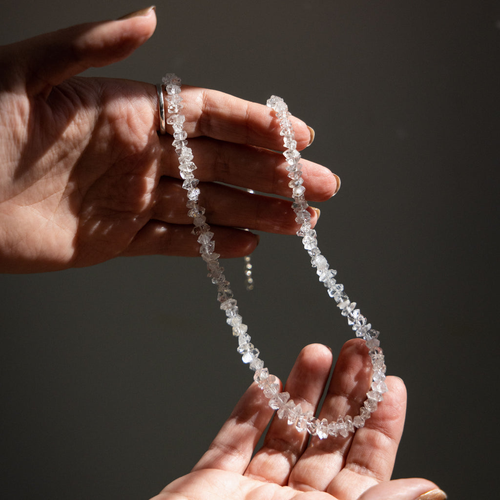 hands holding a herkimer diamond crystal necklace in the sun light