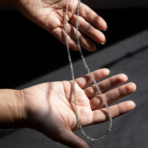 Hands holding a labradorite seed bead crystal necklace in the sun light
